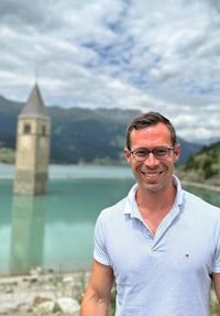 a man standing in front of a lake with a clock tower in the background